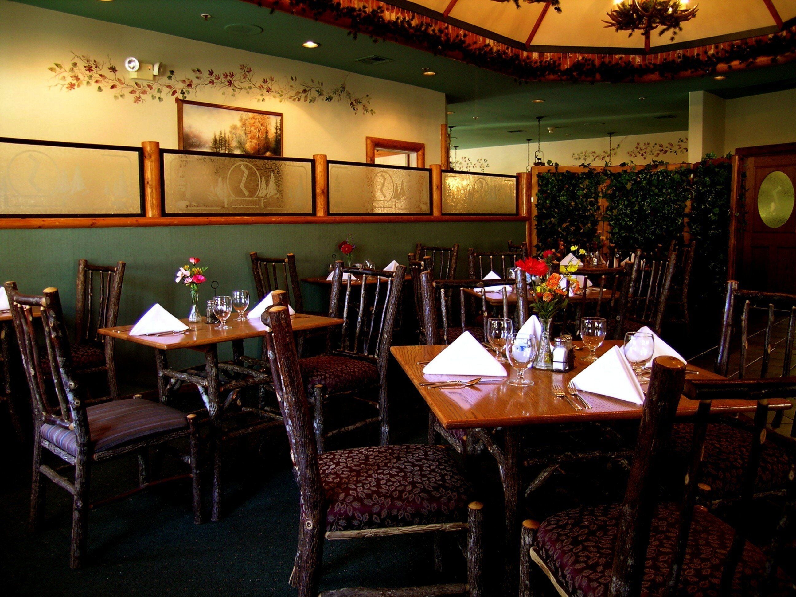 Interior de un restaurante con mesas y sillas de madera, centros de mesa con flores y cuadros en las paredes.