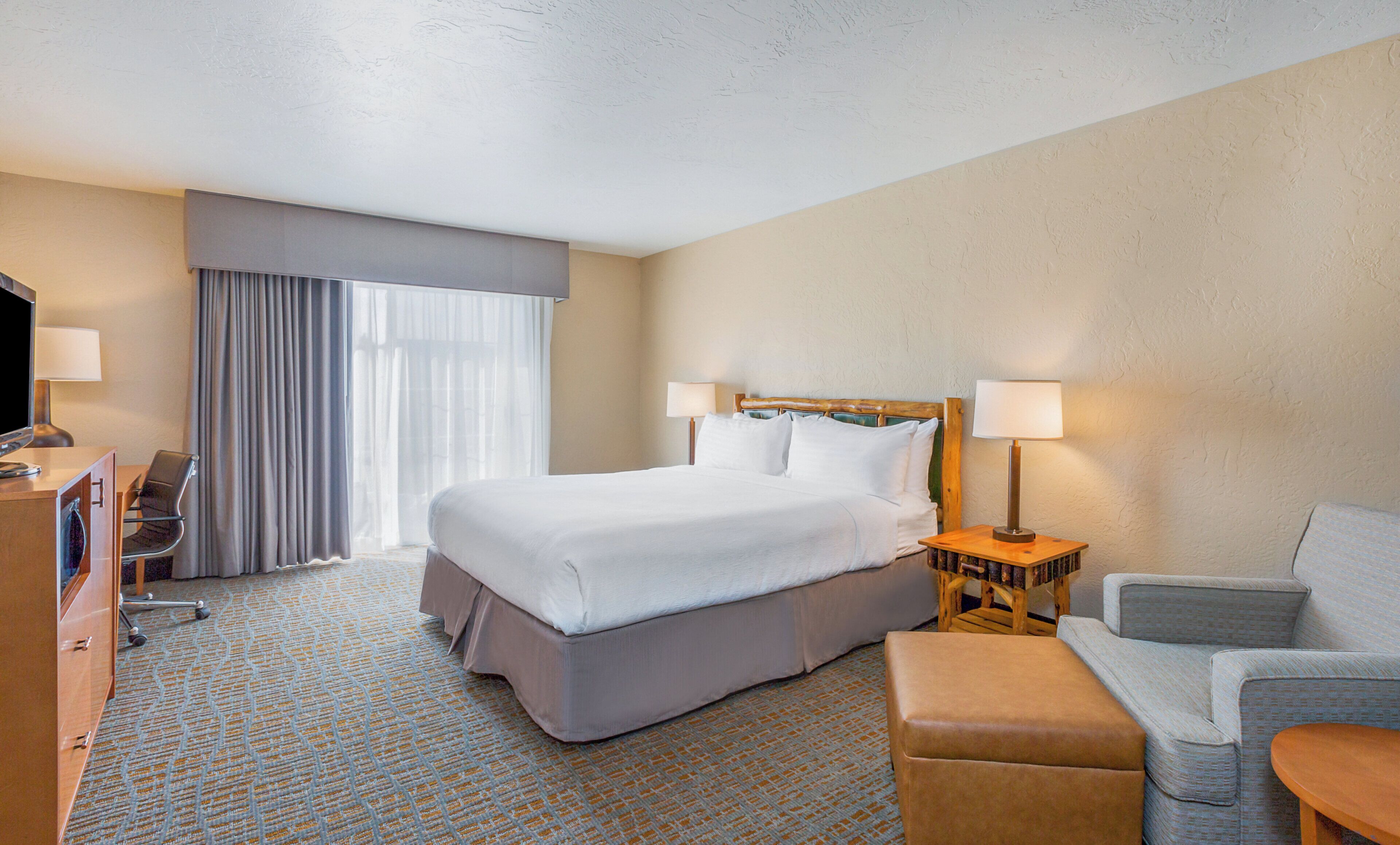 A hotel room with a large bed, two bedside lamps, a television, a desk with a chair, and a sofa.