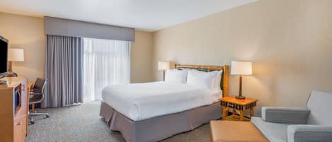 A hotel room with a large bed, two bedside lamps, a television, a desk with a chair, and a sofa.