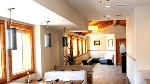 Una habitación de hotel con suelo de madera, un ventanal grande, un sofá, una mesa de comedor con sillas y un espejo.