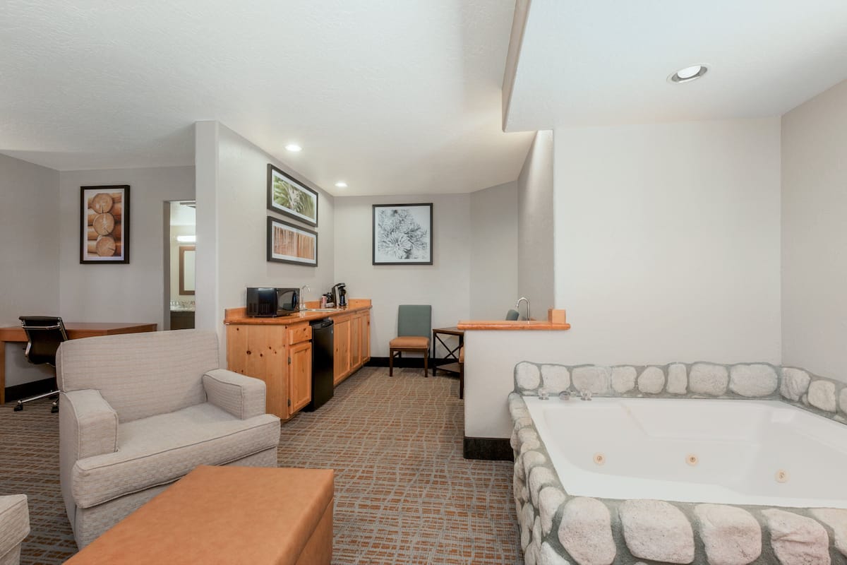 A modern hotel room with a stone bathtub, a sofa, a dining table, and a kitchen area.