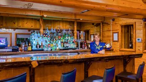A bar area with wooden walls, a variety of liquor bottles, and bar stools.