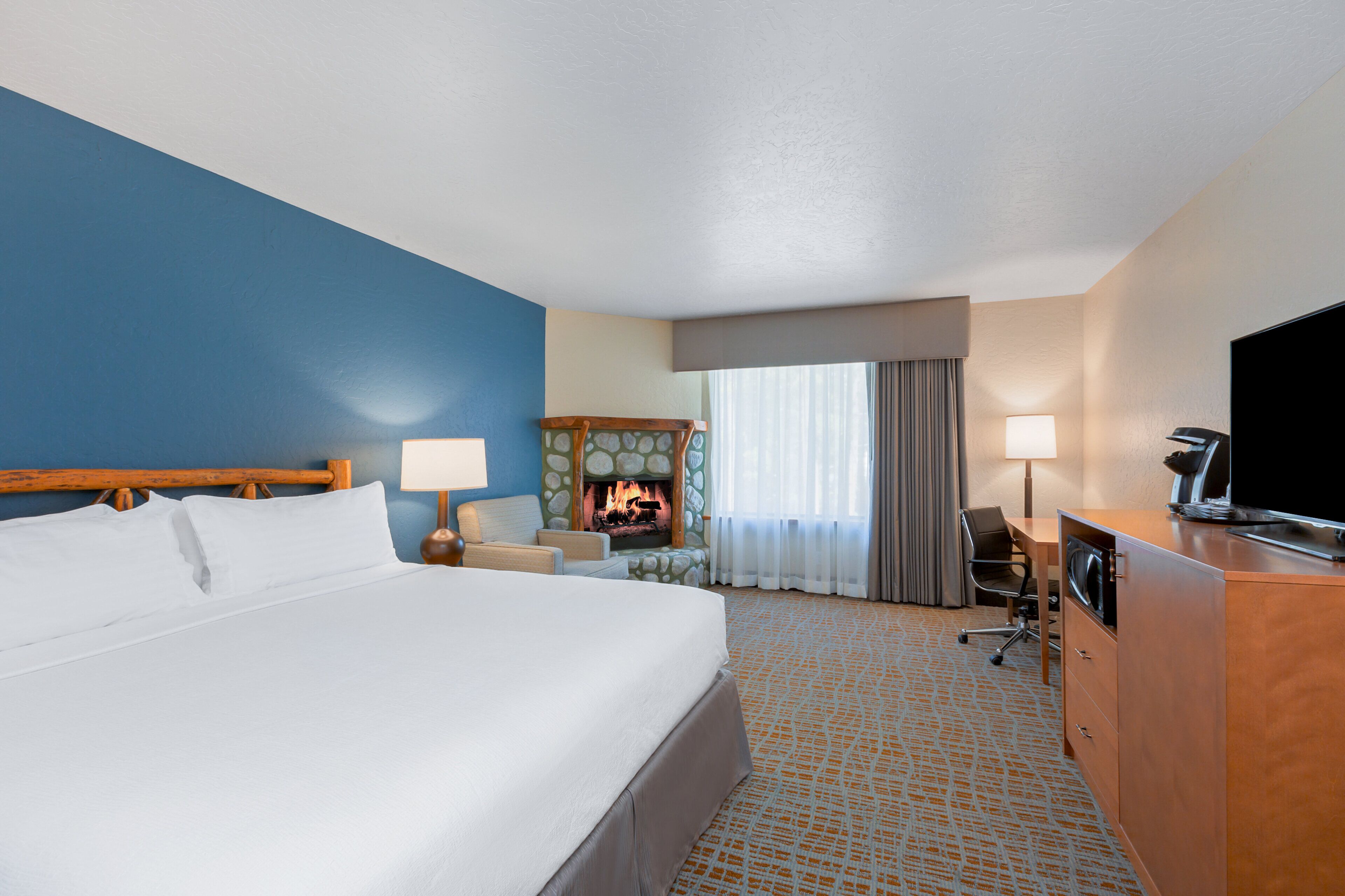 A hotel room with a bed, a desk, a television, and a fireplace.