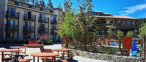 A courtyard with outdoor tables and chairs, a swimming pool, and a multi-story building with balconies.