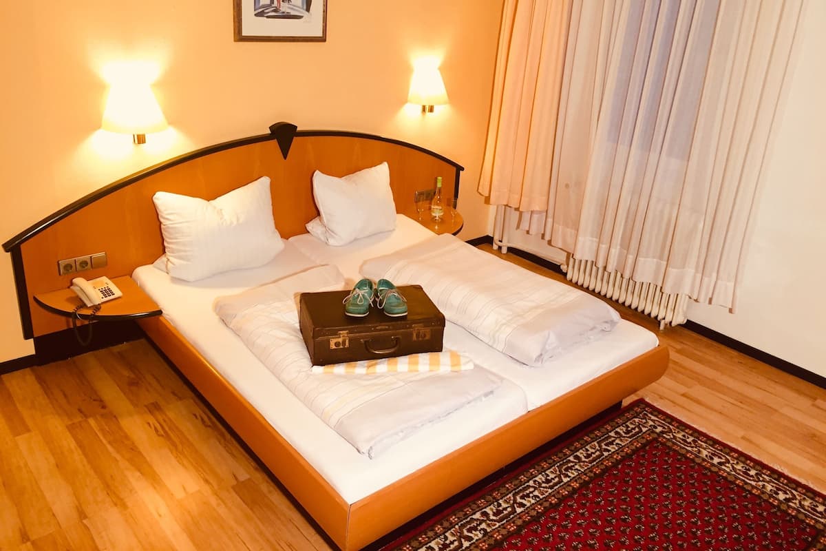 Quarto de hotel com cama, abajures, telefone, mala e tapete.