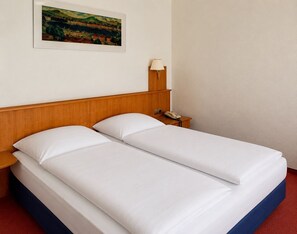 Una cama doble con ropa blanca, un cabecero de madera, una mesita de noche con lámpara y teléfono.