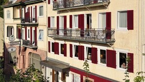A hotel with a traditional European architectural style, featuring multiple balconies and red shutters.