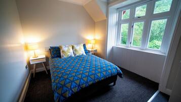 A bedroom with a bed, two bedside lamps, and a window with a view of greenery.