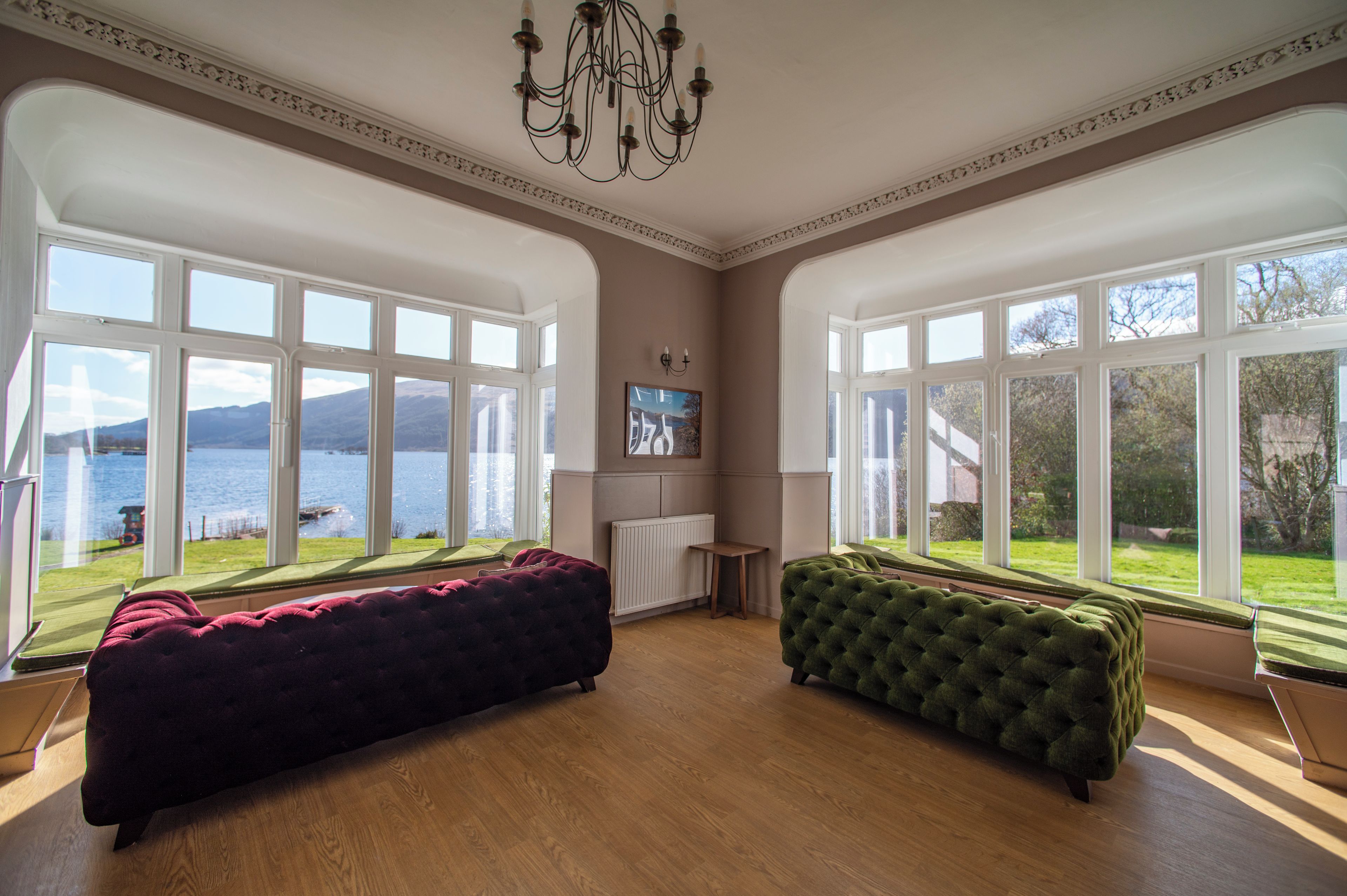 Ein geräumiger Raum mit großen Fenstern, einer Kandelaberleuchte und zwei komfortablen Sofas.