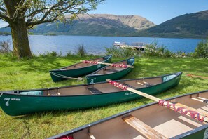 Three green canoes tied to a dock by a tree, with a lake and mountains in the background. - Rowardennan Youth Hostel (Balmaha)