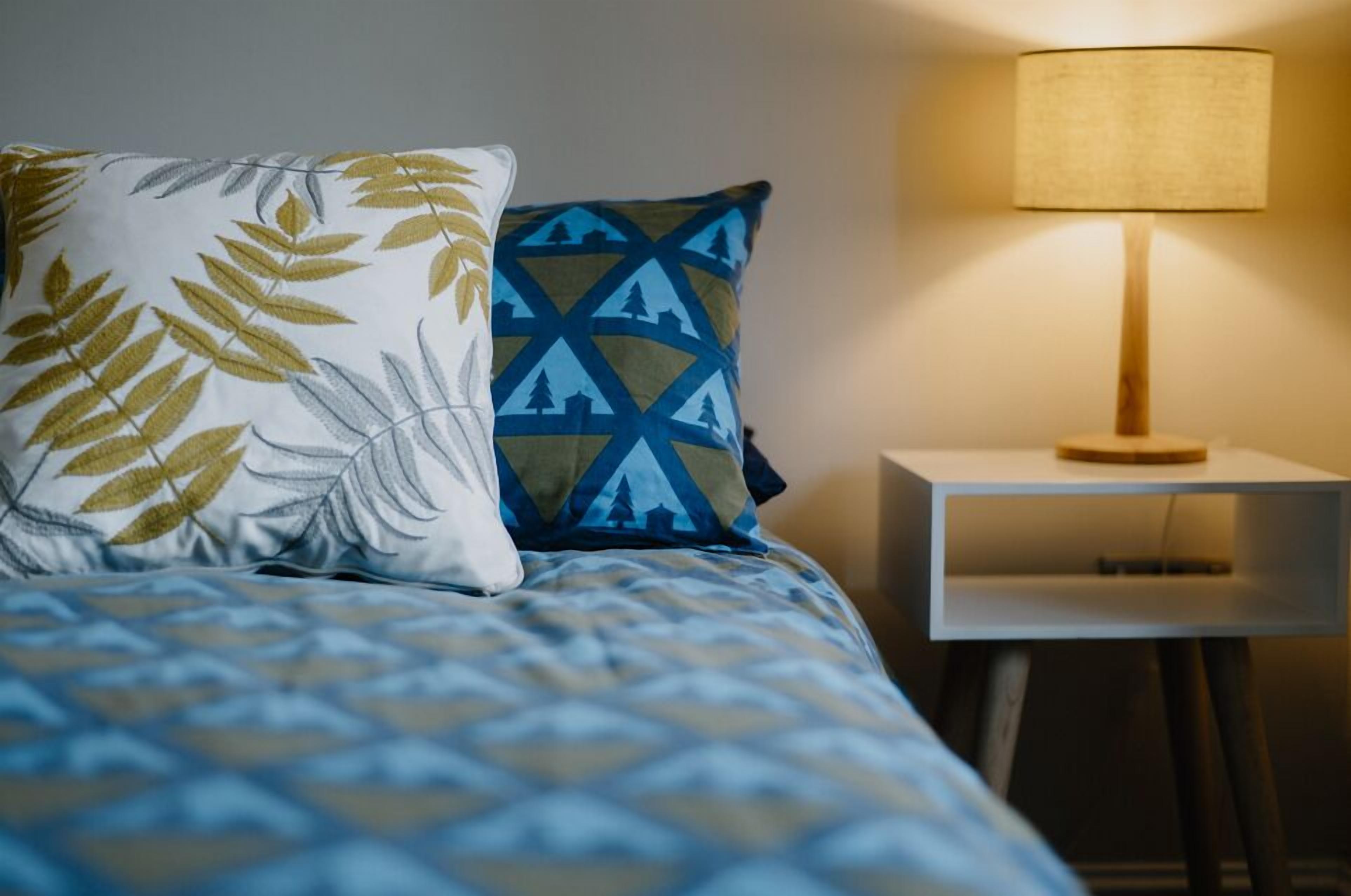 A neatly made bed with patterned bedding, two pillows, and a bedside table with a lamp.