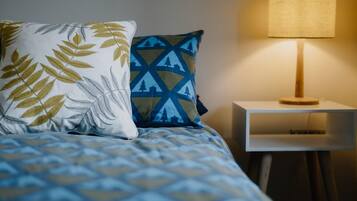 A neatly made bed with patterned bedding, two pillows, and a bedside table with a lamp.