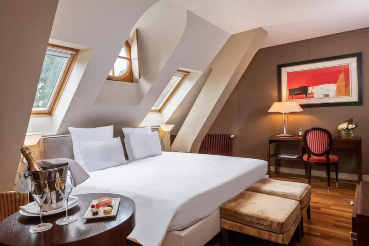 A hotel room with a bed, a small table with a bottle of champagne, glasses, and a plate with snacks.