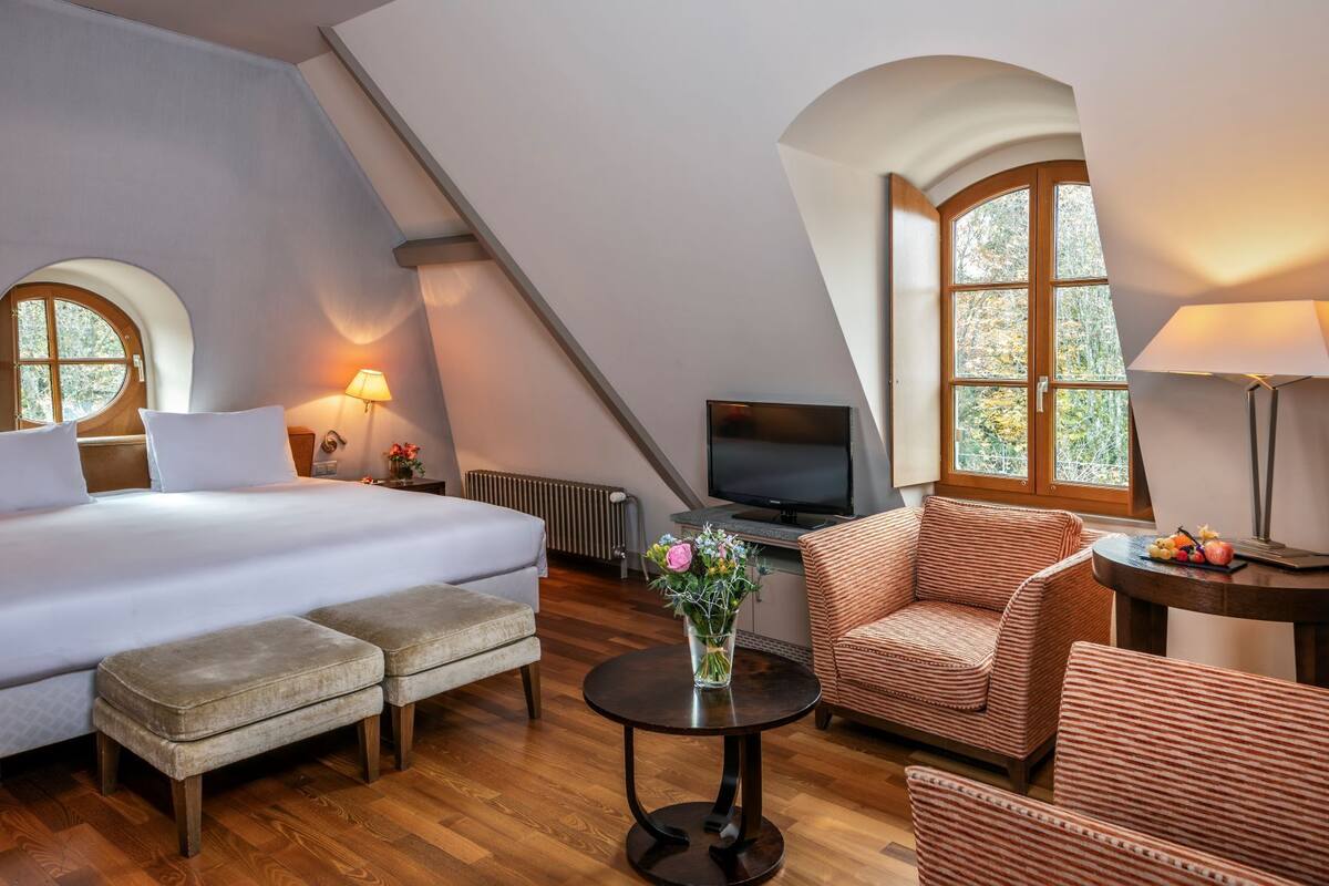 A bedroom with a bed, a TV, a sofa, a table, and a window.