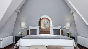 A bedroom with a sloped ceiling, a bed with white bedding, two bedside tables with lamps, and a window with a wooden frame. - Hotel Parc des Eaux-Vives (Geneva)