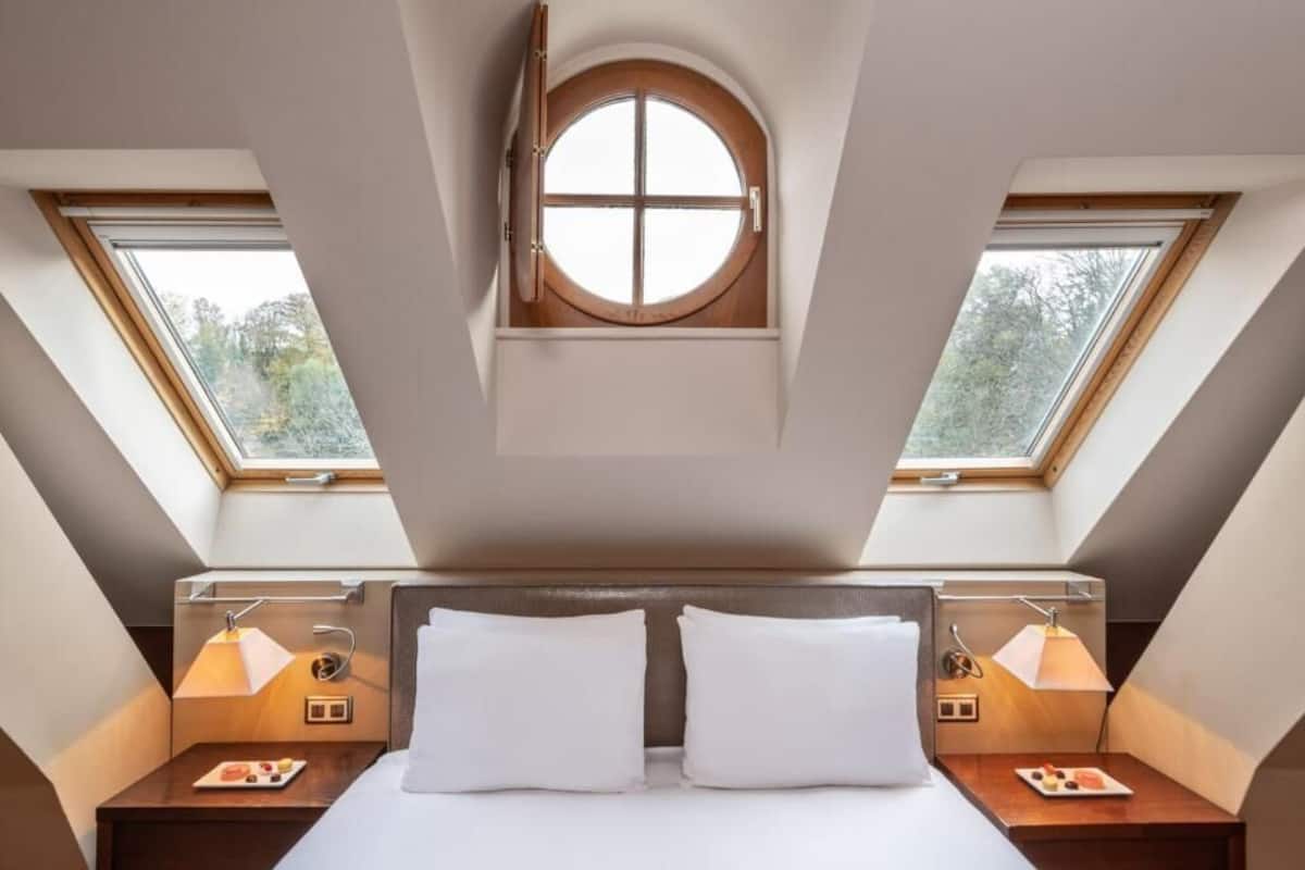 A bedroom with a skylight, two bedside tables with lamps, and a bed with white bedding.