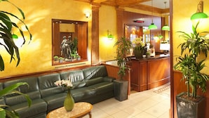 Un hall con un sofá de cuero verde, un mostrador de recepción y plantas en macetas.