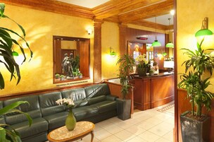 Un hall con un sofá de cuero verde, un mostrador de recepción y plantas en macetas.