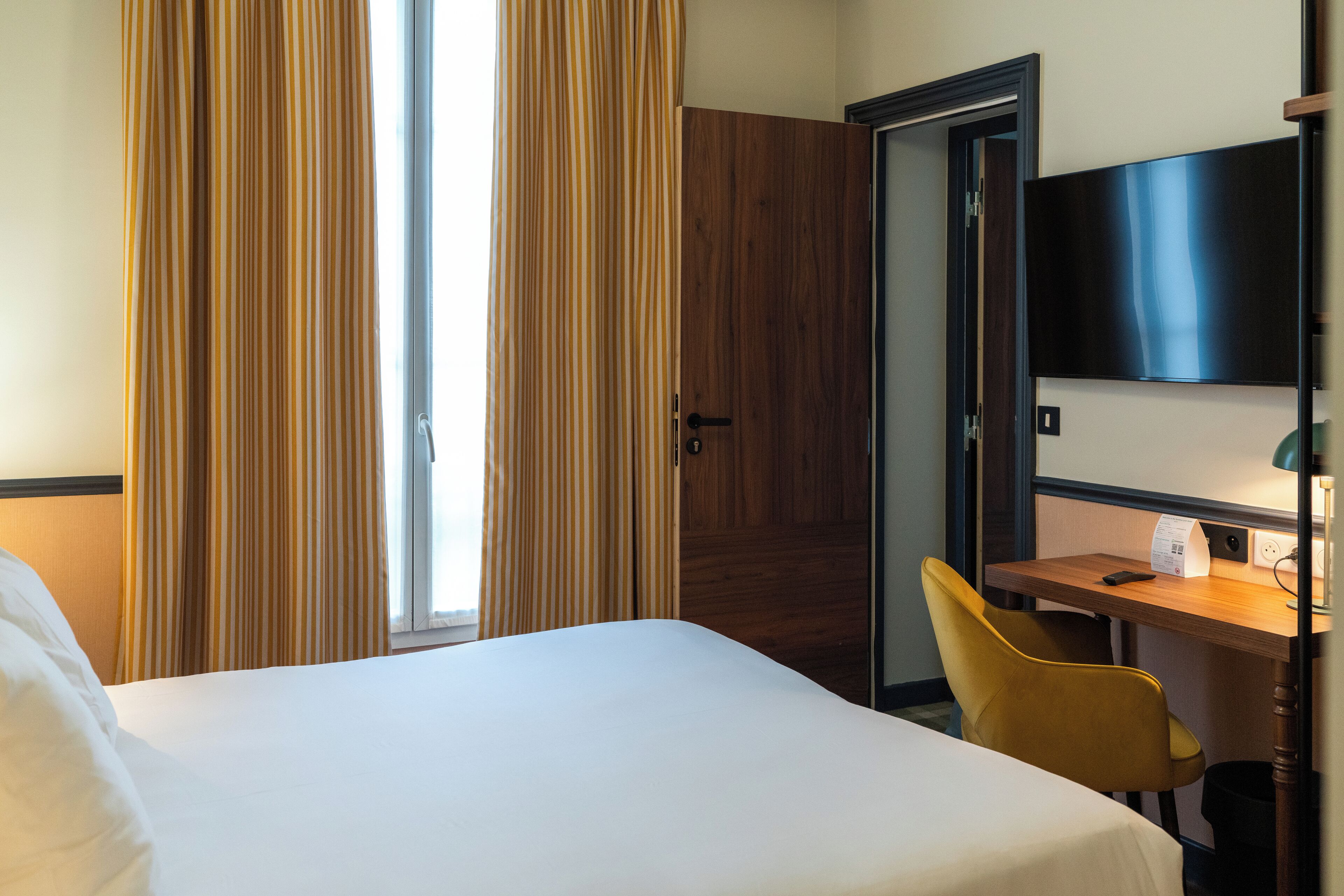 A hotel room with a bed, a desk, a chair, a TV, and a door.
