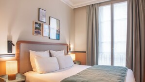 Una habitación de hotel con una cama grande, dos mesitas de noche y un ventanal con cortinas.