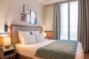 Una habitación de hotel con una cama grande, dos mesitas de noche y un ventanal con cortinas.