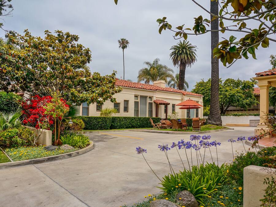 A well-maintained garden with a variety of plants and flowers, a patio area with outdoor furniture, and a building with a tiled roof.