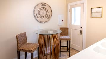A bathroom with a glass table, two wicker chairs, a woven stool, a door, and a framed picture on the wall.