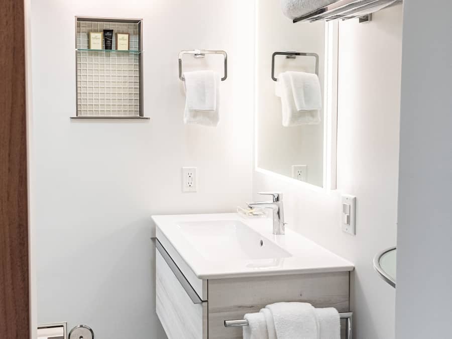 A modern bathroom with a white vanity, a large mirror, and a towel rack.