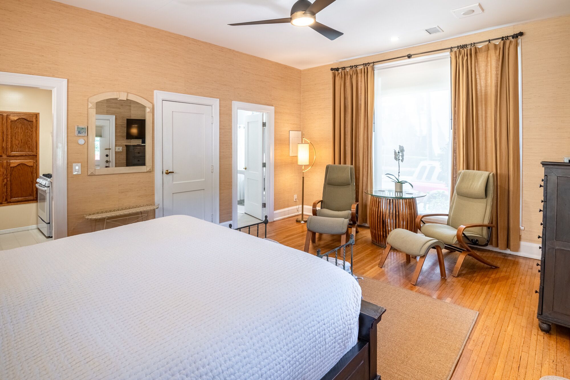 Een hotelkamer met een groot bed, twee stoelen, een bijzettafeltje, een lamp en een kledingkast.