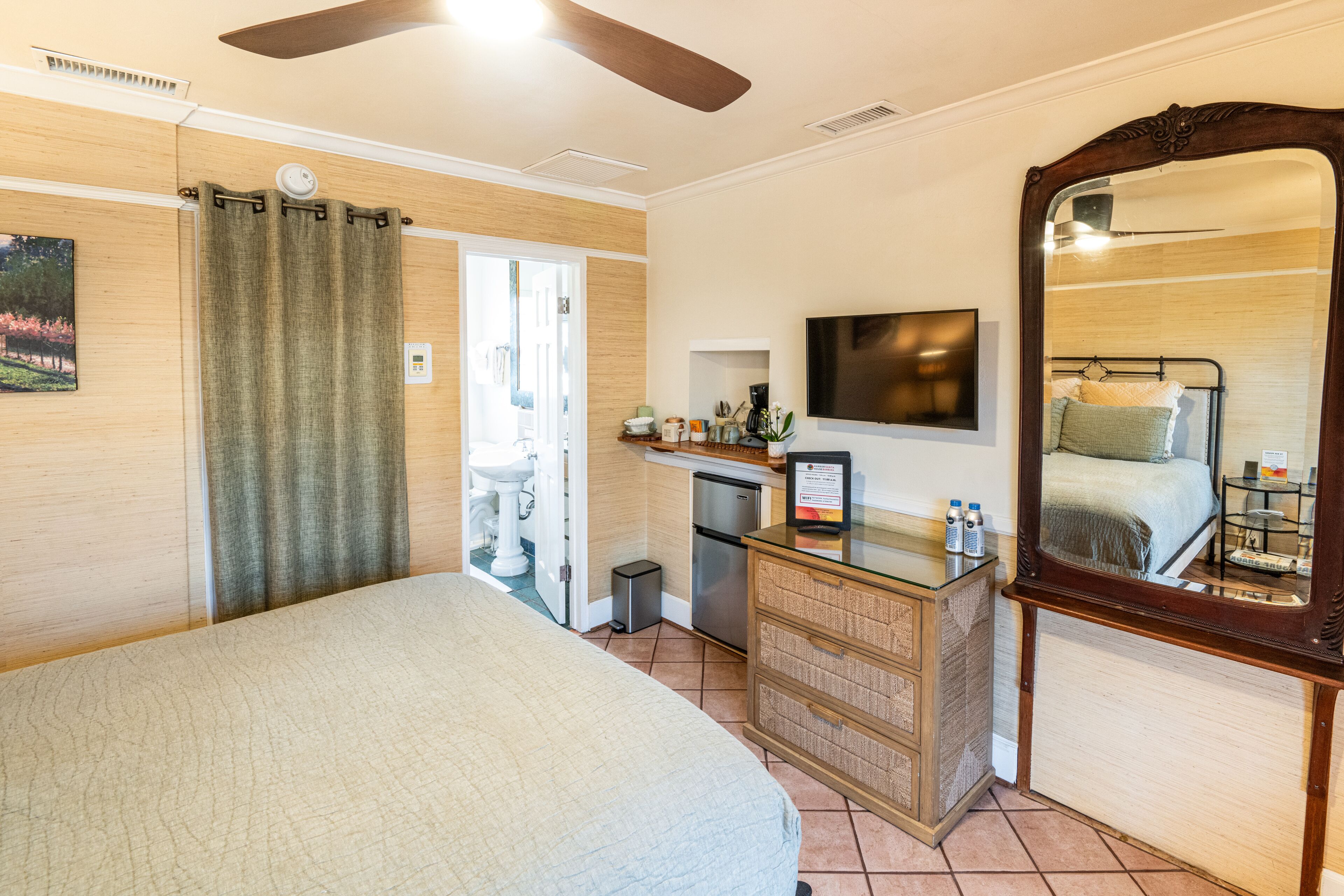 A hotel room with a bed, a dresser, a mirror, a television, and a kitchenette.
