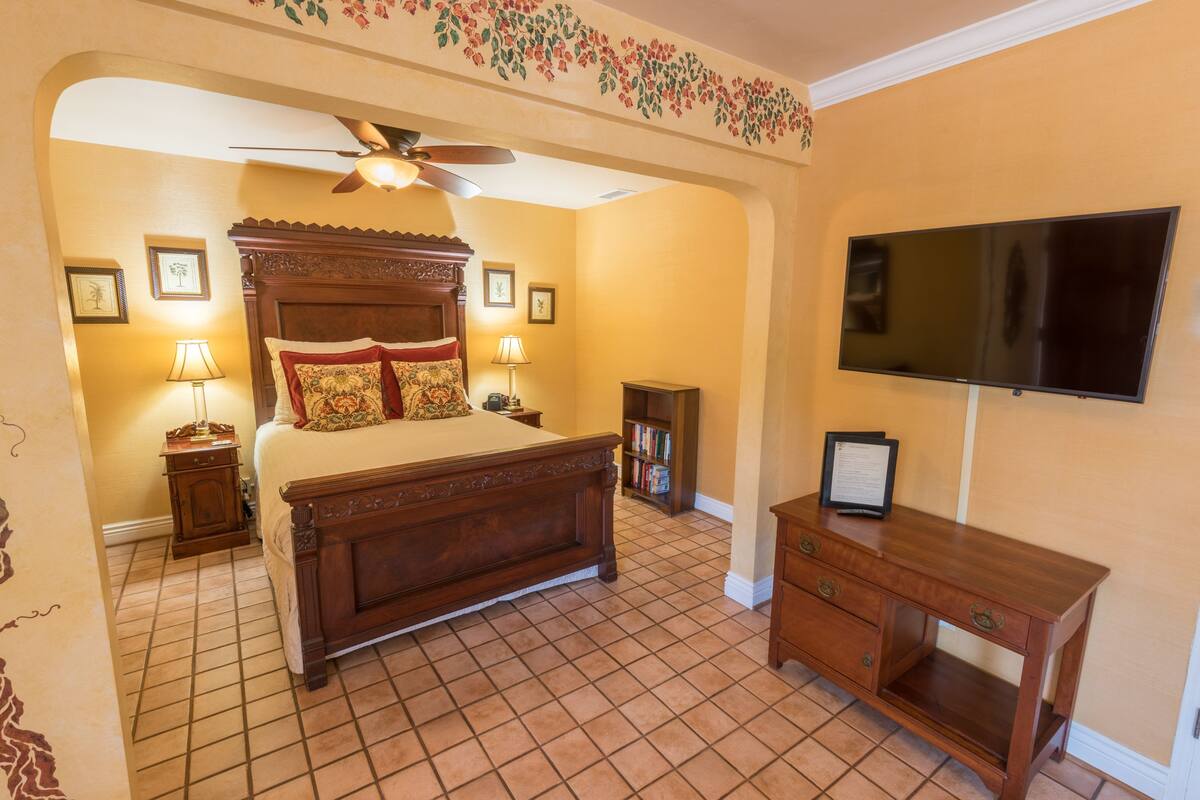 Ein Schlafzimmer mit einem hölzernen Bett, einem Deckenventilator, einem Fernseher und einem Bücherregal.