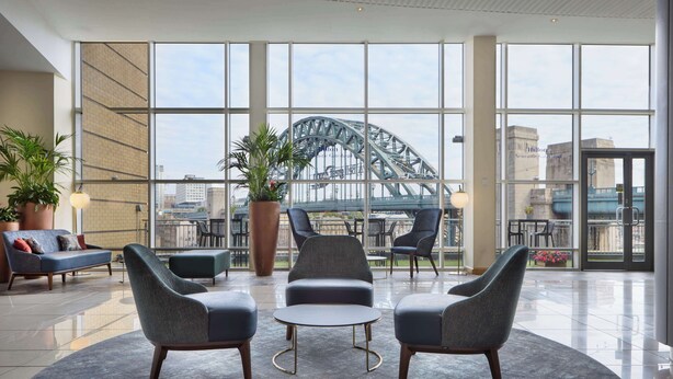 A spacious lobby with modern seating, large windows, and a view of a bridge. - Hilton Newcastle Tyne Bridge (Gateshead)