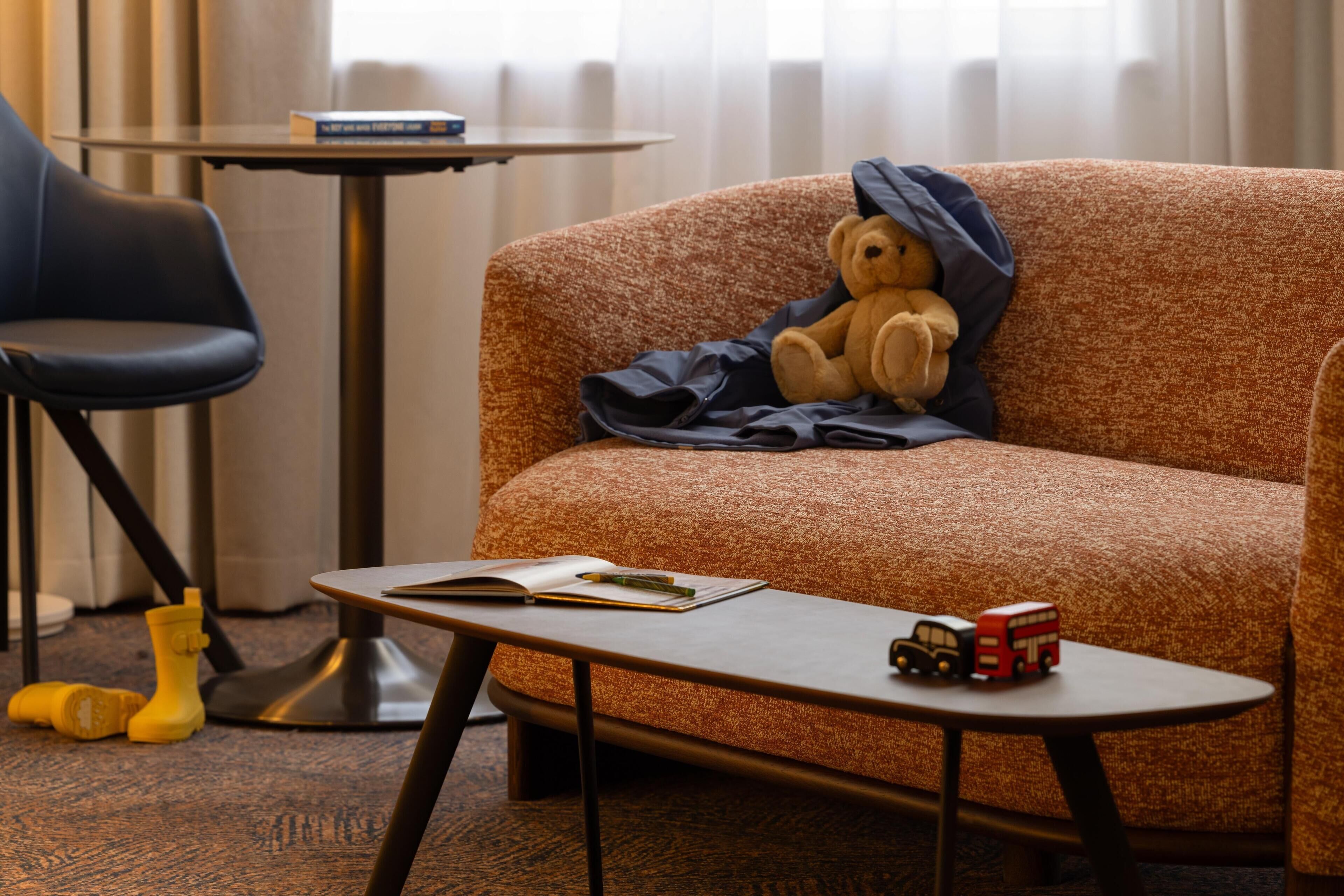 Una habitación acogedora con sofá, una mesita, un osito de peluche y un autobús de juguete.