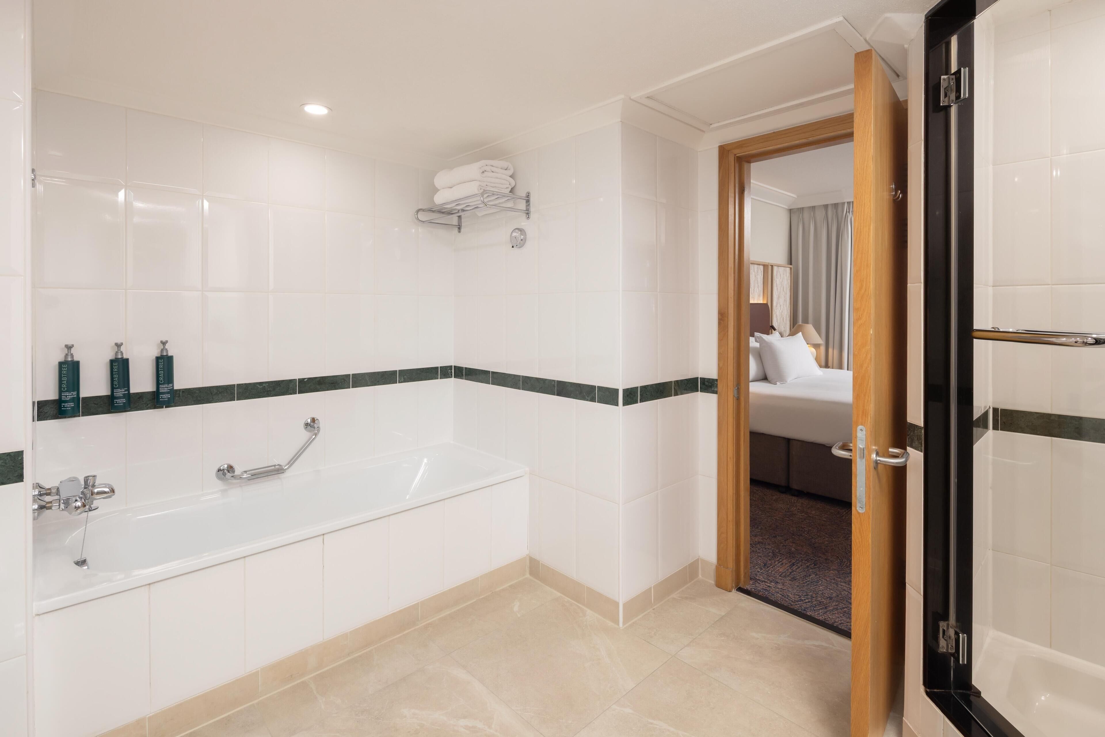 A modern bathroom with a bathtub, a shower, and a toilet. There are toiletries on the wall and a towel rack.