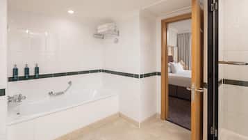 A modern bathroom with a bathtub, a shower, and a toilet. There are toiletries on the wall and a towel rack.