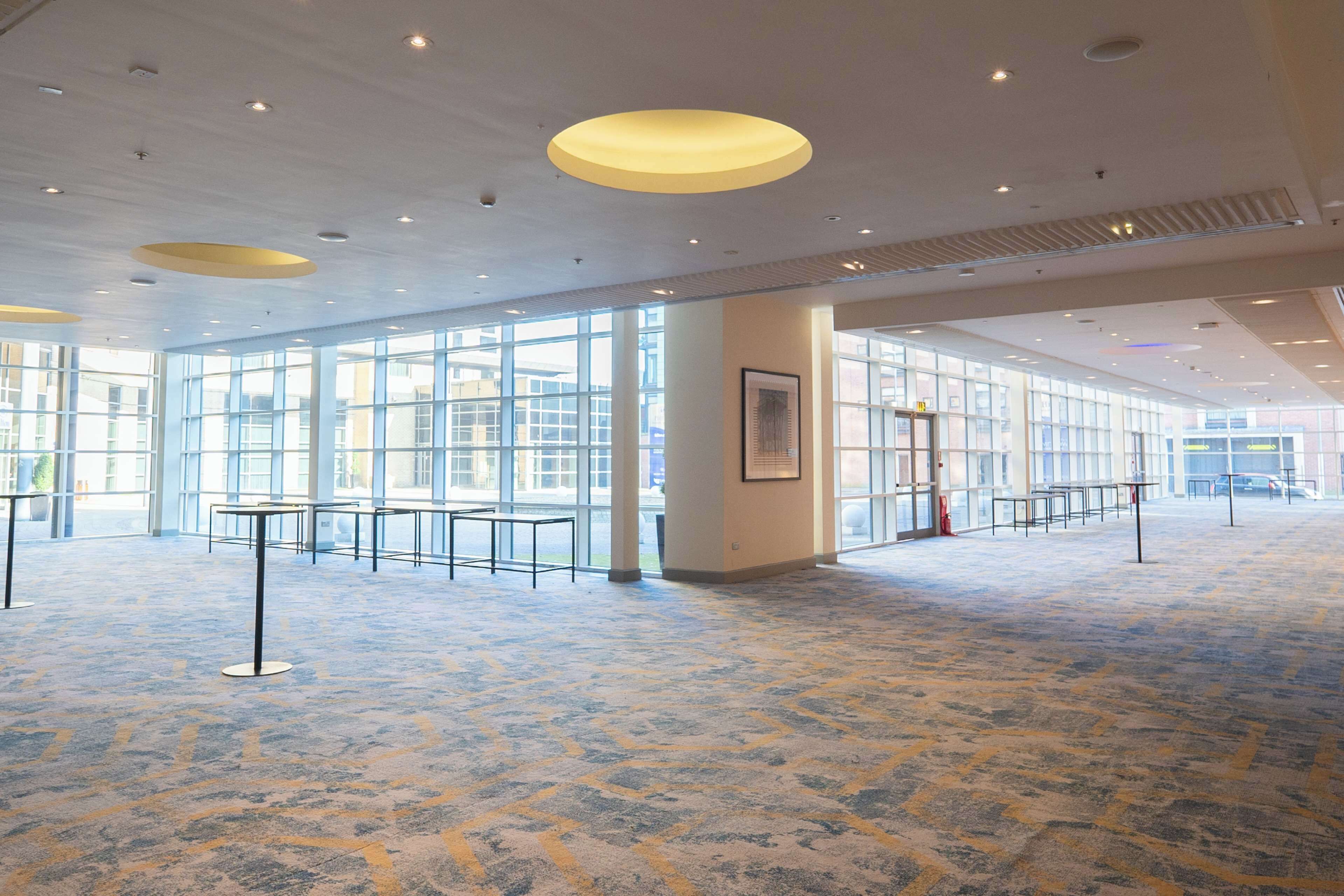 A spacious indoor area with large windows, a patterned carpet, and multiple tables and chairs.