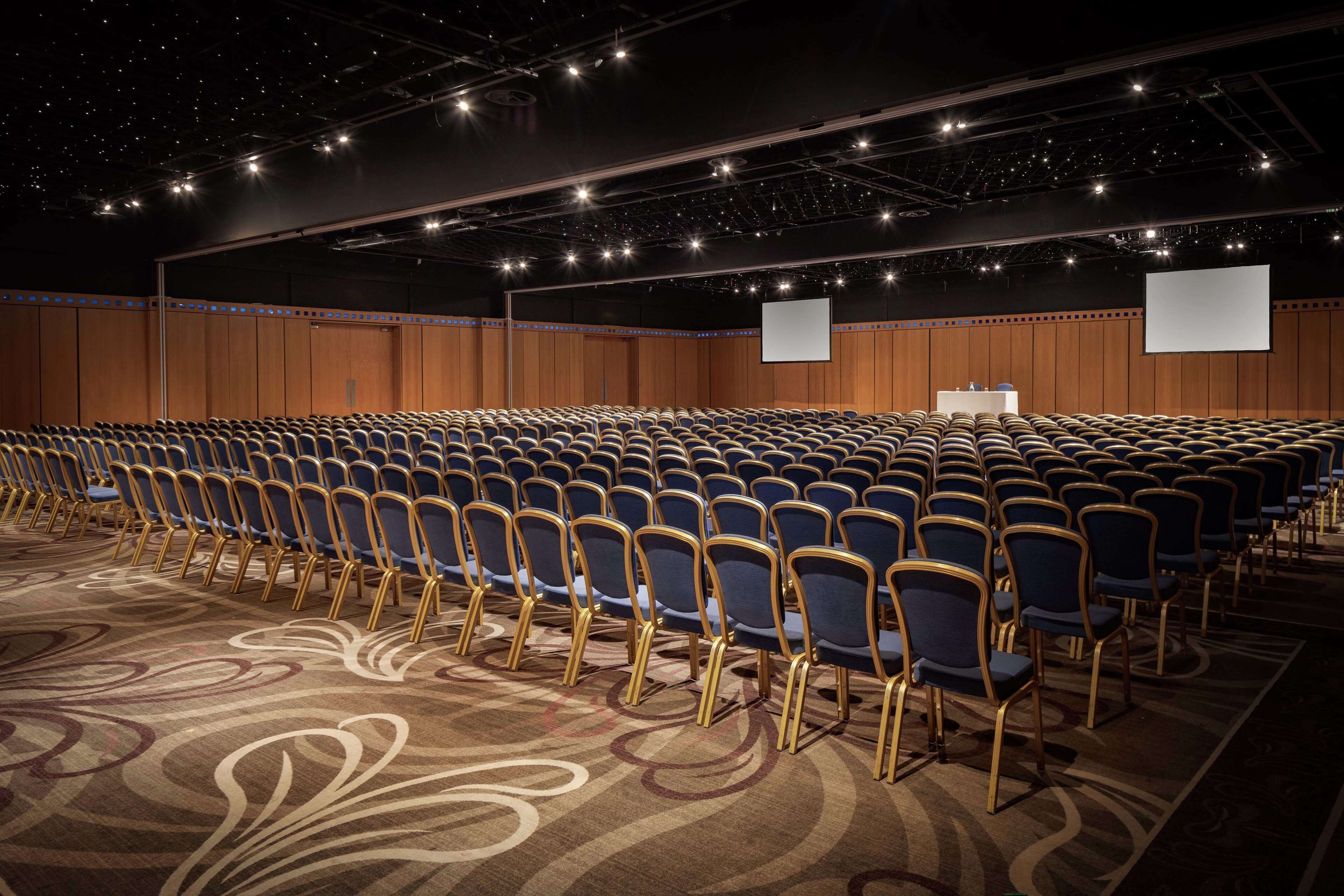 A large conference room with rows of blue chairs and a carpeted floor.