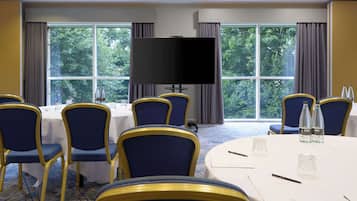 A conference room with a large flat-screen TV, round tables, and blue chairs.