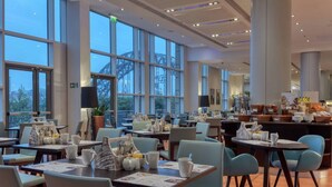 A modern dining area with large windows, tables with menus, and a buffet counter. - Hilton Newcastle Tyne Bridge (Gateshead)