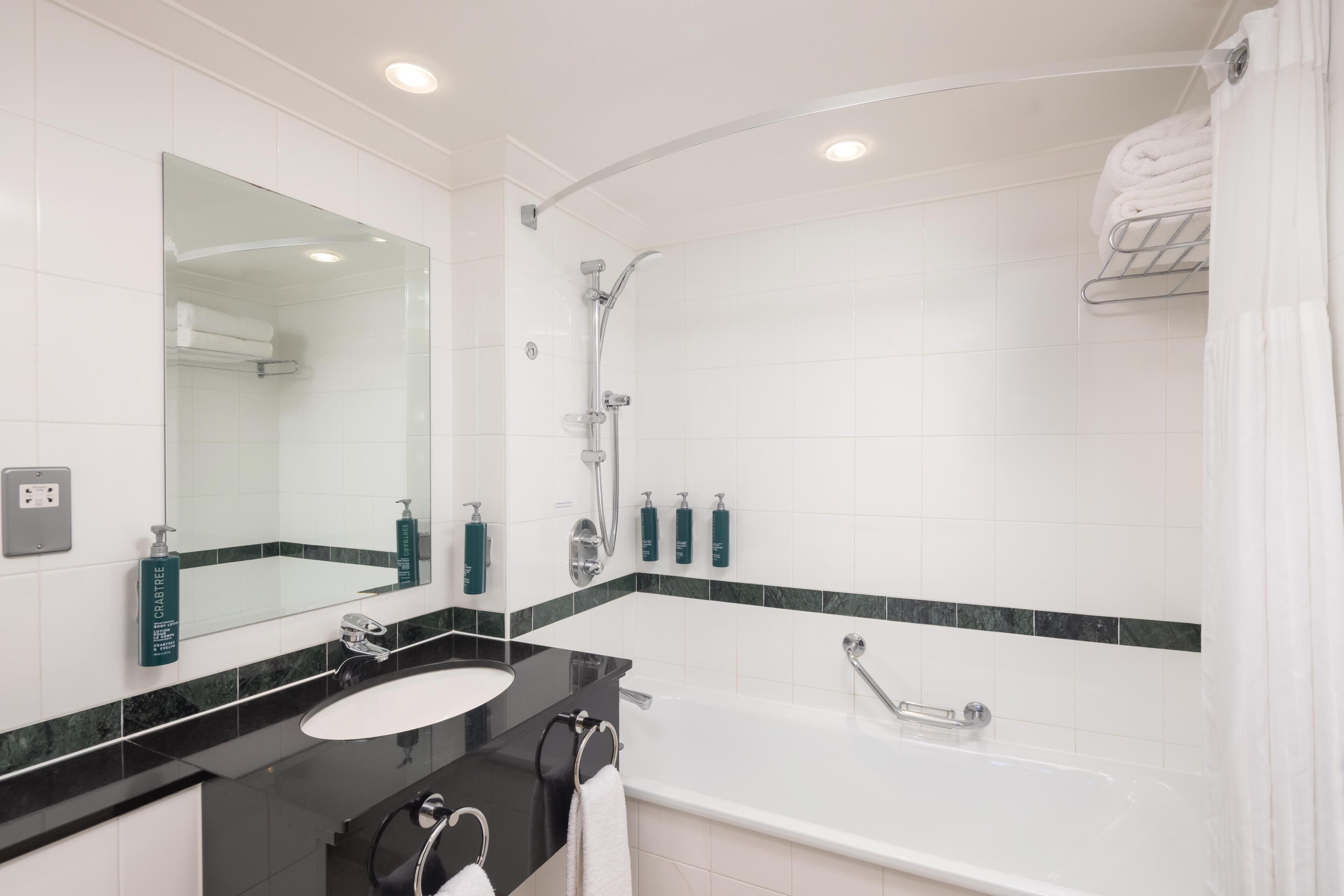 Une salle de bain moderne avec un plan de toilette noir, un lavabo blanc et un grand miroir. Elle comprend un espace douche avec une porte en verre et une baignoire.