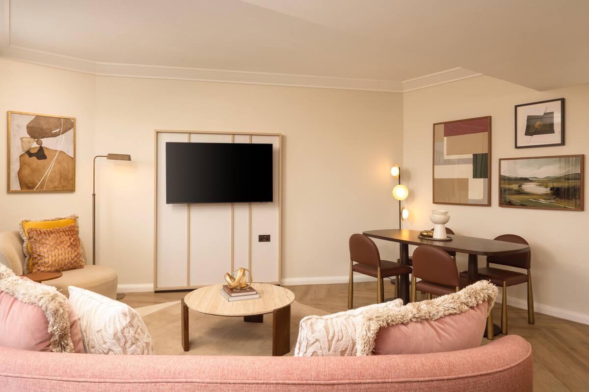 A living room with a flat-screen TV, a round coffee table, a dining table with chairs, and a sofa.