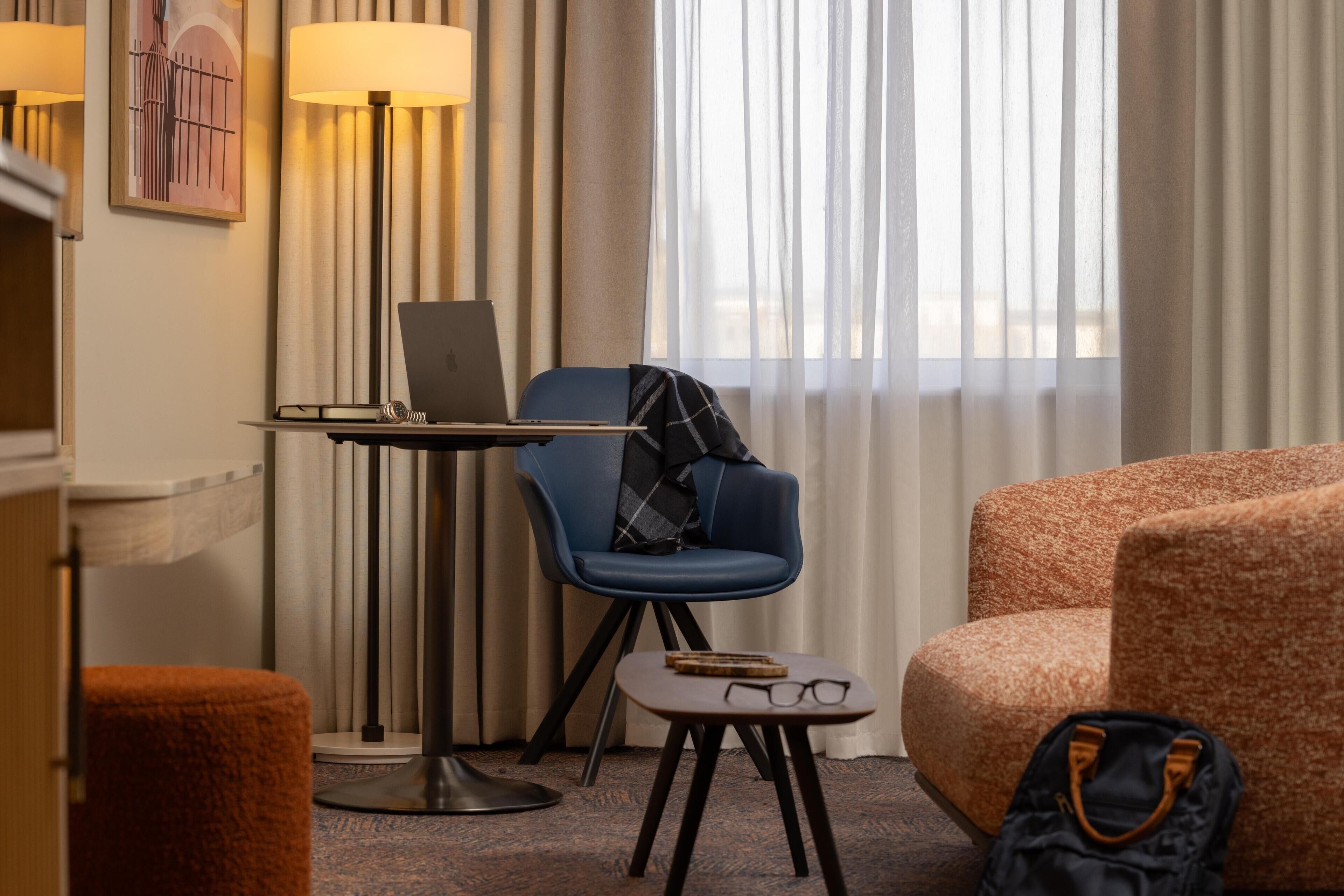Een hotelkamer met een bureau, laptop, blauwe fauteuil en een gestreept sofa.