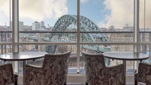 A room with two round tables and four patterned chairs, large windows with a view of a cityscape and a prominent bridge. - Hilton Newcastle Tyne Bridge (Gateshead)