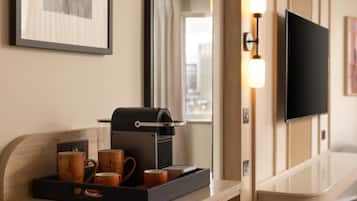 A hotel room with a coffee machine, mugs, a tray, a flat-screen TV, and a framed picture on the wall.