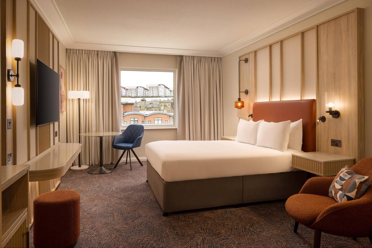A hotel room with a large bed, a desk, a chair, and a TV.