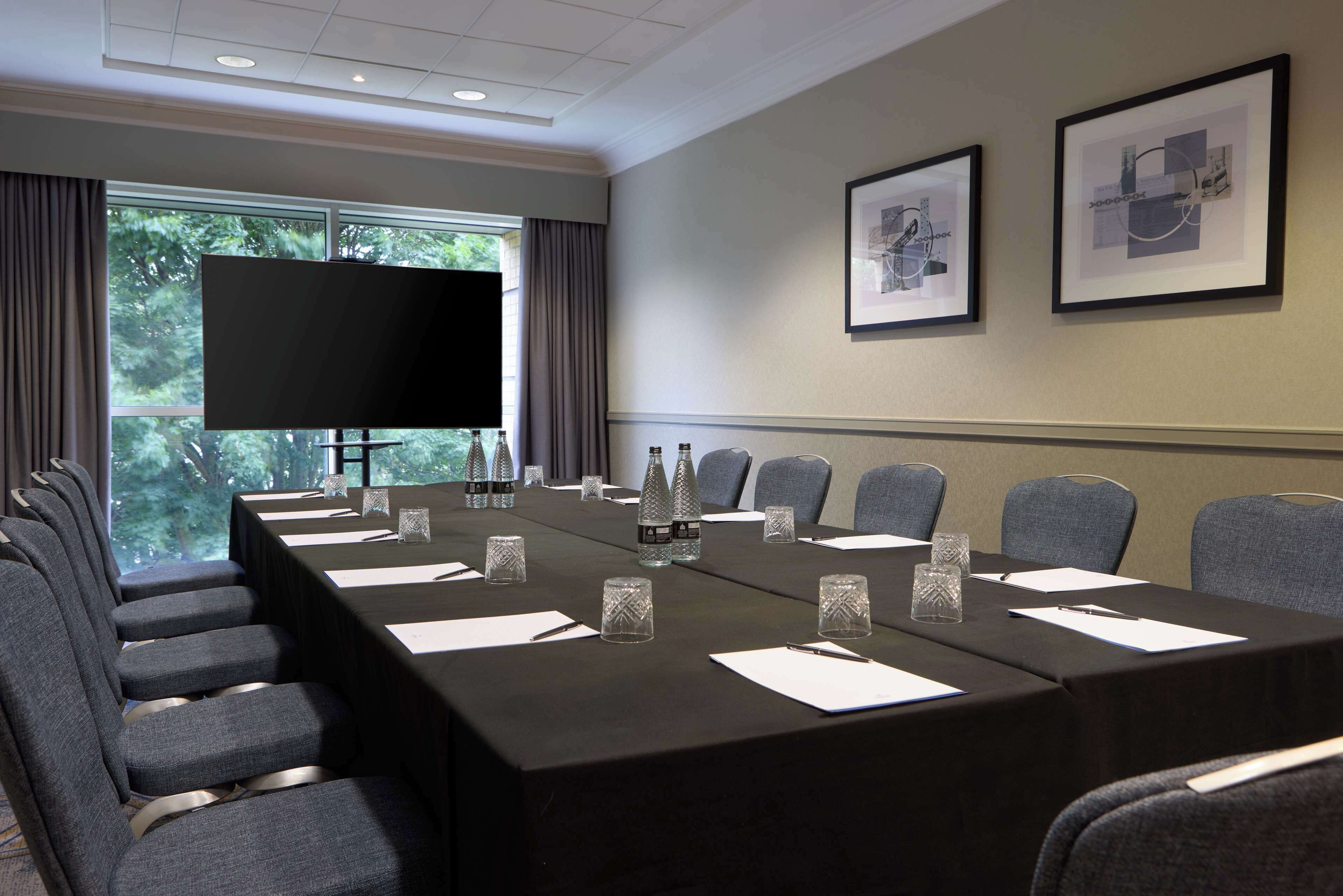 Una sala conferenze con un lungo tavolo, sedie, un televisore e quadri appesi al muro.