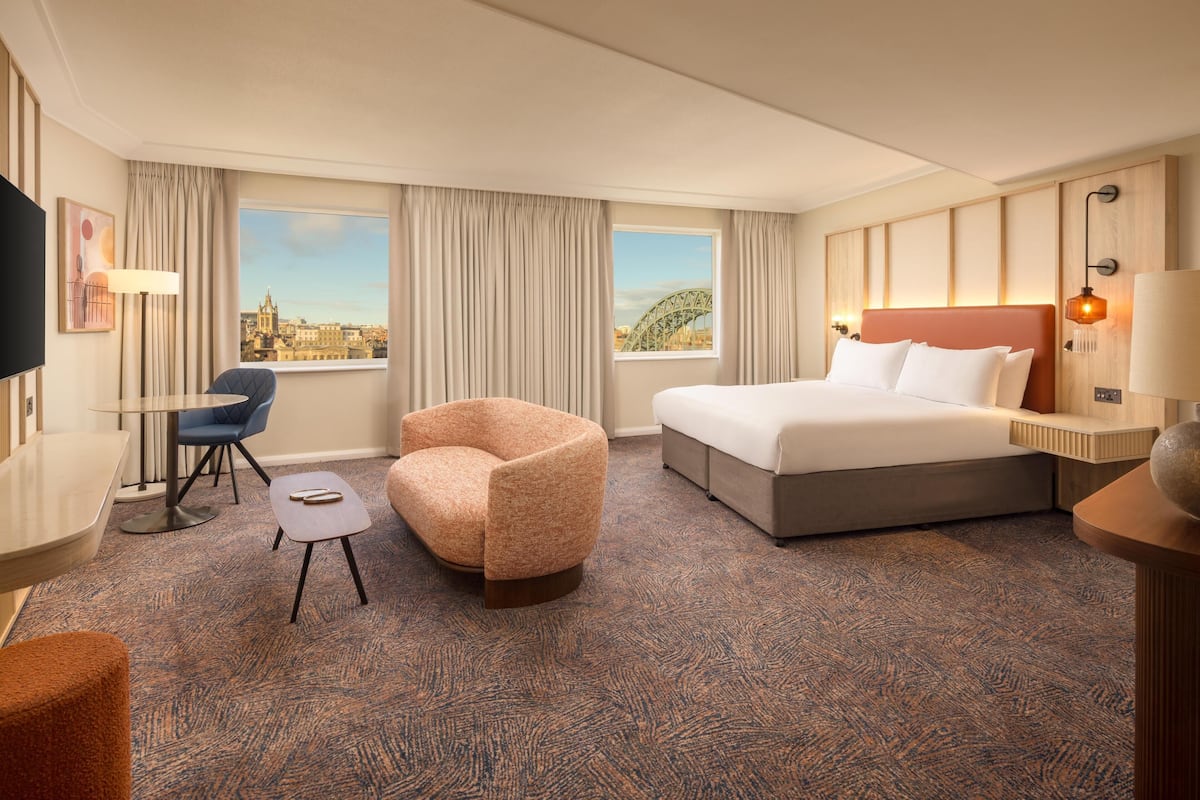 A hotel room with a bed, a desk, a chair, and a view of a cityscape.