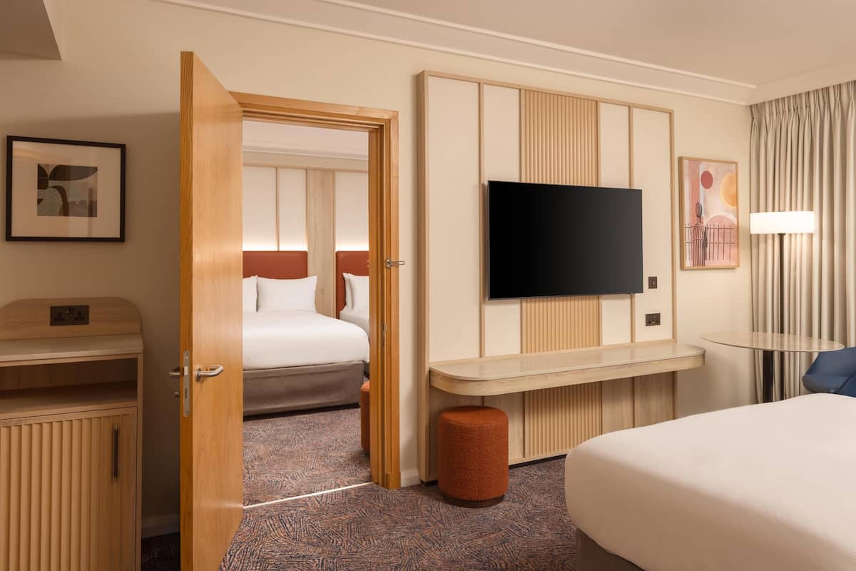 A hotel room with a bed, a TV mounted on the wall, a desk, and a wardrobe.