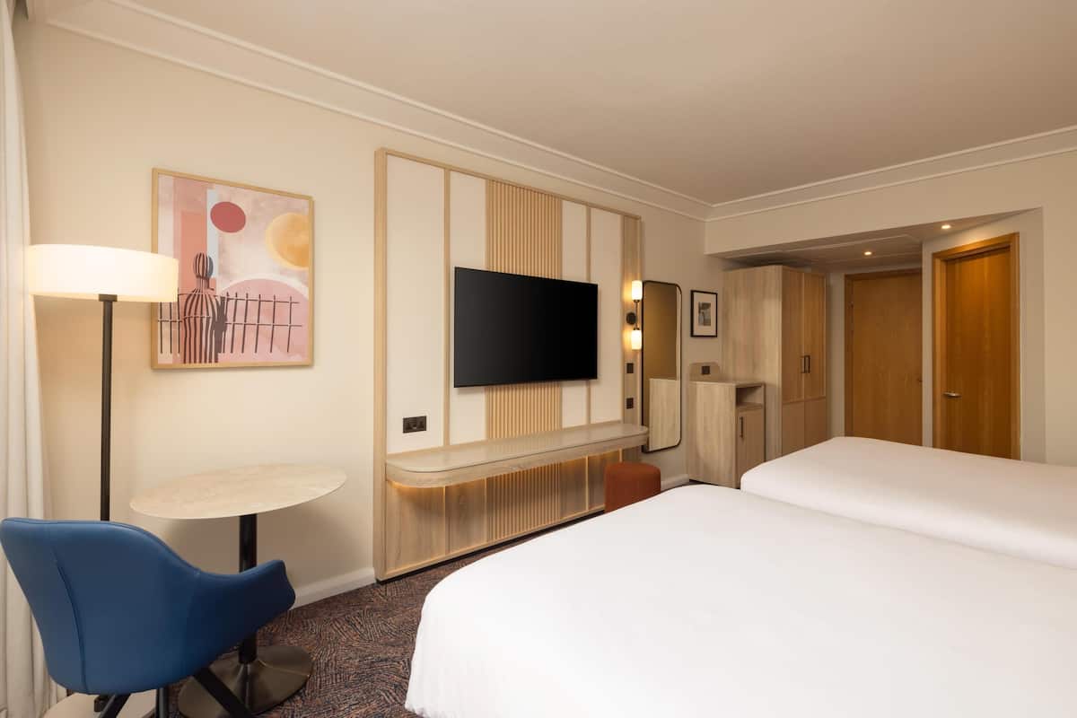 A hotel room with a bed, a desk with a chair, a flat-screen TV mounted on the wall, and a wardrobe.