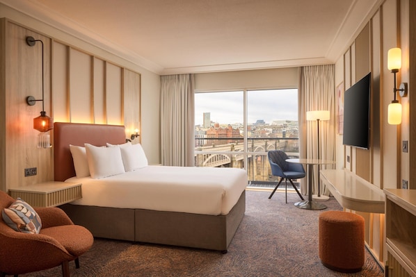 Habitación de hotel con una cama grande, un escritorio, una silla, un televisor y vistas a la ciudad.